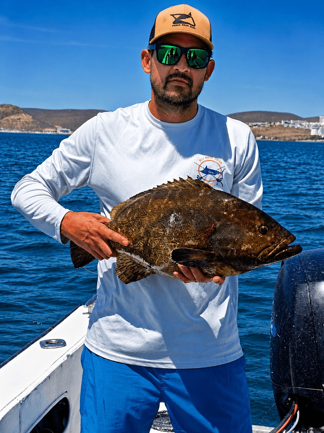Capitán con una cabrilla recién pescada, con La Paz al fondo